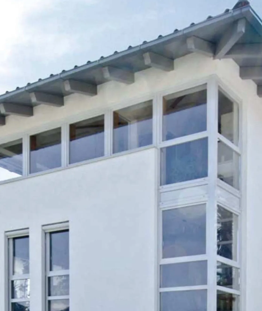 Über Eck geführte weiße Fensterelemente an einer hellen Fassade unter einem weit auskragenden Dach
