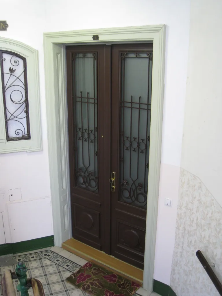 Zweiflügelige dunkelbraune Sicherheitstür mit Ziergittern vor Mattglas, eingebaut in einem Stiegenhaus